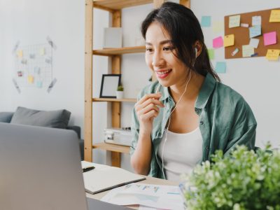 Asia businesswoman using laptop talk to colleagues about plan in video call while smart working from home at living room. Self-isolation, social distancing, quarantine for corona virus prevention.
