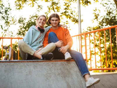 Young smiling boy and girl happily looking in camera spending time together in skatepark